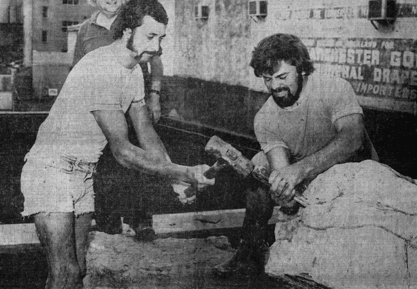 Two men breaking a rock with a hammer and chisel